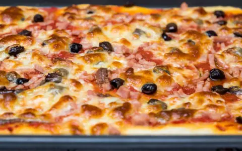 Une pizza rectangulaire garnie de jambon, d'olives et de fromage fondant. Parfait pour savoir que faire avec une pâte à pizza rectangulaire !