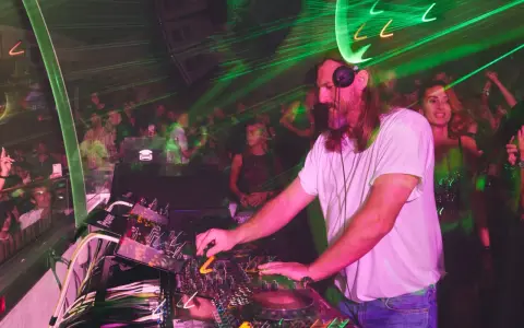 DJ w białej koszulce grający na konsoli w klubie z zielonymi laserami.