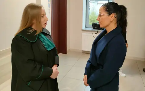 Prawniczka w todze rozmawia z kobietą w granatowym płaszczu.