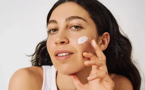 Frau mit zu Akne neigender Haut trägt eine leichte Creme auf.