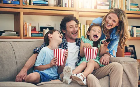 Rodzina śmieje się do rozpuku, jedząc popcorn podczas oglądania filmu dla całej rodziny.