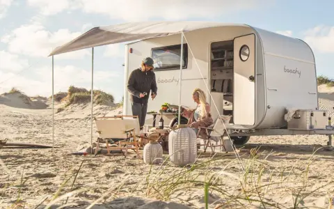 Ett par njuter av en stranddag med sina tyska husvagnar. Solen skiner och sanddynerna skapar en vacker bakgrund.