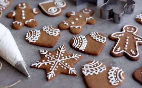 Pepparkakshus och hjärtan dekorerade med vit kristyr. En sprits med kristyr ligger bredvid.