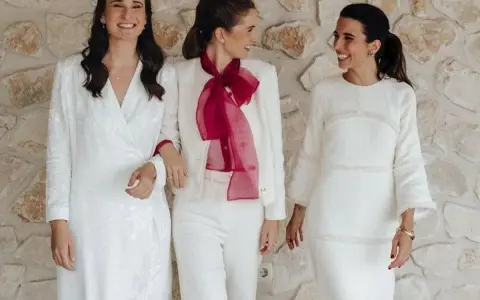 Tres mujeres sonríen vestidas de blanco, demostrando que se puede ir de blanco a un bautizo.