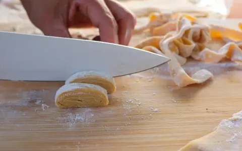 Hand schneidet frisch zubereitete, selbstgemachte Pasta auf einem Holzbrett.