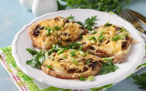 Schab w plastrach pieczony w piekarniku z pieczarkami i serem, posypany szczypiorkiem.