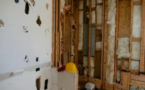 Chantier en cours, murs ouverts révélant l'isolant. Attention, la laine de bois peut présenter un danger si mal manipulée. Casque et gants de protection à proximité.