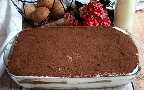 Tiramisù pronto, con 250 gr di mascarpone, pronto per essere gustato. Ingredienti freschi come uova e fiori decorano la tavola.