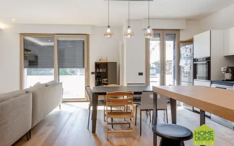 Un soggiorno luminoso con un divano, tavolo da pranzo e cucina a vista. Un moderno sopraluce illumina l'ambiente.