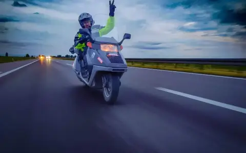 Karta motorowerowa w akcji! Kierowca w kasku i kamizelce odblaskowej pozdrawia, jadąc skuterem po autostradzie.