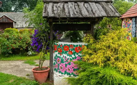 Kolorowa studnia z ludowymi wzorami kwiatowymi, otoczona zielenią i krzewami róż. Idealne miejsce na wakacje na wsi.