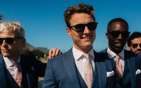 Four men in blue suits with pink ties and sunglasses, embodying a "dress to impress" dress code for a sunny outdoor event.