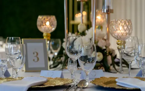 Elegancko nakryty stół weselny z kieliszkami, złotymi talerzami i świecami. Czy warto personalizować każdy element wesela od serwetek po etykiety? Tak!