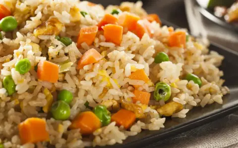 Arroz tres delicias con guisantes y zanahoria en un plato negro.