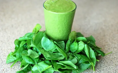 Un verre de smoothie vert entouré d'épinards frais, parfait pour un régime sans lectine.
