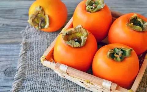 Frische, orangefarbene Kaki-Früchte liegen in einem kleinen Korb auf grobem Leinen. Kaki gesund und lecker.