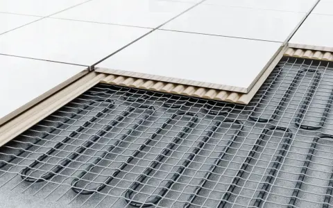 Coupe d'un sol carrelé montrant le système de chauffage au sol : câbles chauffants sous une couche isolante et un support, puis les carreaux.