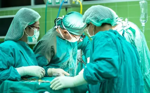 Zespół chirurgów w zielonych fartuchach i czepkach przeprowadza skomplikowaną operację głosu.