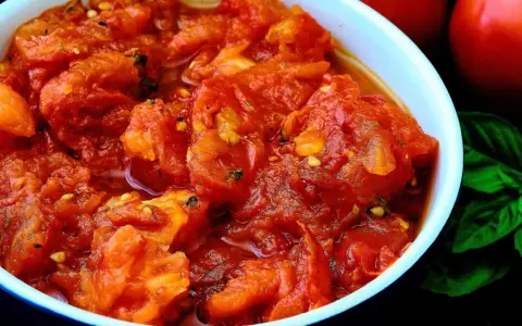 Un tazón de tomates picados, jugosos y vibrantes, con un toque de albahaca fresca y dos tomates enteros al fondo. Un bonito con tomate listo para disfrutar.