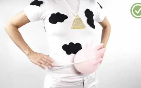 Persona con un disfraz vaca casero: camiseta blanca con manchas negras, collar de campana dorada y un globo rosa simulando la ubre.