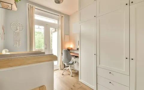 Un angolo studio in camera da letto, con scrivania, sedia girevole e armadio bianco.