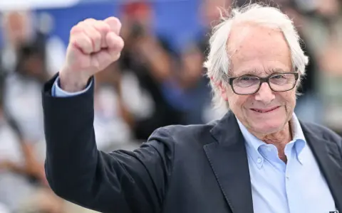 Ken Loach, regista inglese famoso, alza il pugno in segno di vittoria.