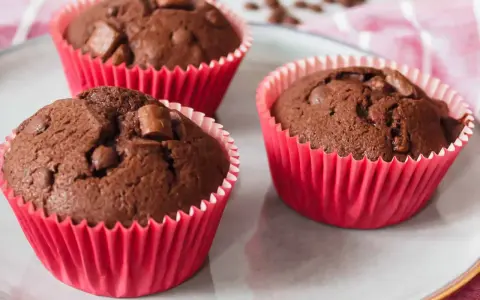 Drei saftige Schokomuffins mit Schokostückchen in roten Papierförmchen, perfekt für Kinder.
