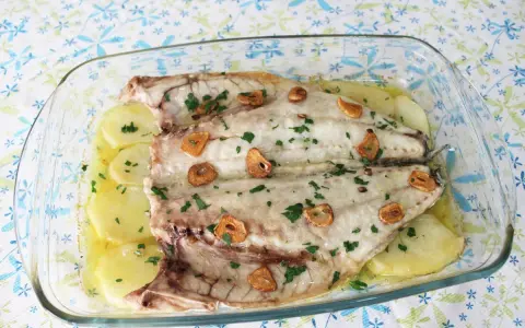 Lubina a la espalda horneada con patatas, ajo y perejil en una fuente de cristal.