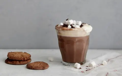 En härlig varm choklad med choklad, toppad med marshmallows och chokladspån. Bredvid står några chokladkakor.