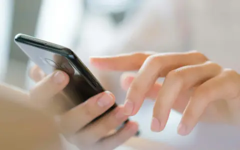 Dłonie wpisują numer referencyjny przesyłki na ekranie smartfona.