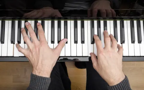 Dłonie grające akordy na pianinie. Muzyka płynie z klawiszy.