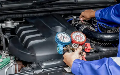 Mecánico realiza carga de gas al aire acondicionado de un coche, usando manómetros para verificar la presión.