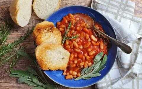 Fagioli all'uccelletto in umido con pomodoro, serviti con pane tostato e erbe aromatiche. Perfetti per scoprire cosa abbinare ai fagioli all'uccelletto.