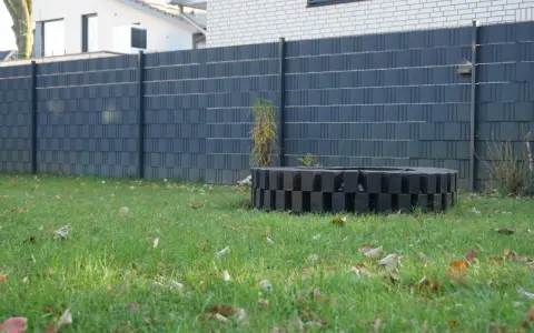 Moderner Sichtschutzzaun, der sich gut zum zaun selber bauen billig eignet. Ein dekorativer Kreis aus schwarzen Steinen im Garten.