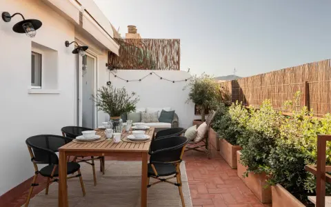 Acogedora terraza de 25 metros cuadrados con mesa de madera, sillas negras, sofá, plantas y luces decorativas.