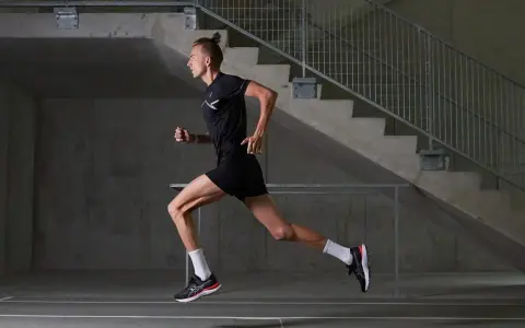 Mężczyzna w czarnym stroju sportowym biegnie, czerpiąc z biegania w tlenie. Dynamiczna sylwetka na tle betonowych schodów.