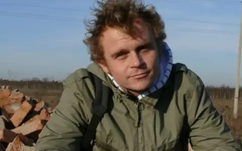 Piotr Rogucki, w otoczeniu gruzu, z charakterystyczną fryzurą, jakby inspirowany swoimi utworami.