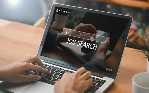 Ręce wpisują "JOB SEARCH" na laptopie. Praca wre, szukamy nowych możliwości.