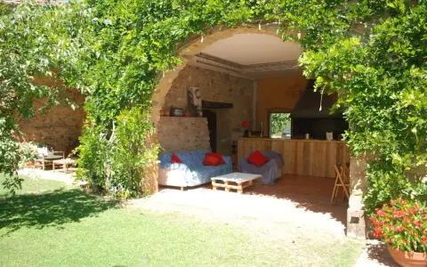 Un jardín con una madreselva planta cubriendo un arco de piedra. Dentro, sofás y una barra de madera.