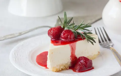 Ein Stück cremige Philadelphia Torte mit Erdbeersauce und frischen Erdbeeren, garniert mit Rosmarin.