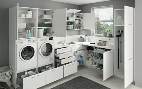 Ein heller, moderner kleiner Hauswirtschaftsraum mit Waschmaschine, Trockner, Spüle und viel Stauraum in weißen Schränken.