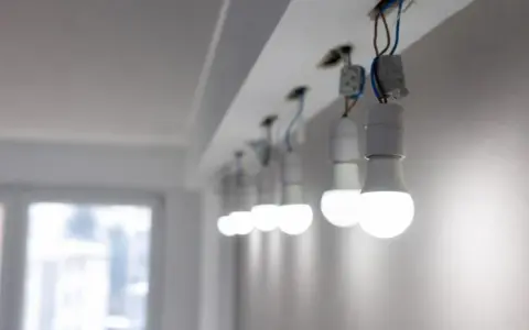 Rząd białych żarówek LED, wiszących na przewodach, świeci jasno, mimo że instalacja wygląda na nieukończoną.