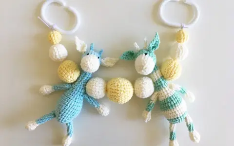 Crocheted giraffes with white and yellow beads hanging from white plastic rings.