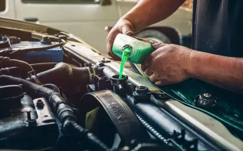 Mecánico rellenando refrigerante verde en el radiador de un coche, solucionando una posible fuga de gas aire acondicionado.