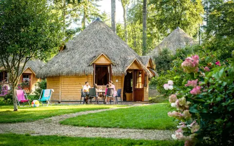 Famille profitant d'un repas en terrasse devant leur chalet en chaume, parfait pour des vacances scolaires en Bretagne.