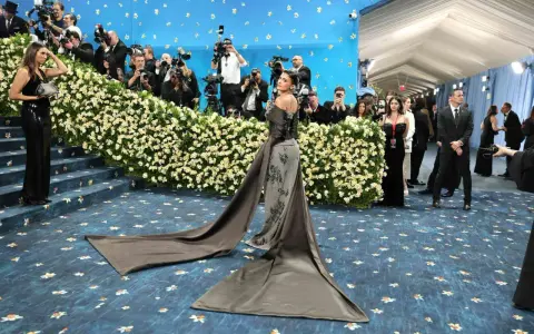 Kylie Jenner arrives at the Met Gala in a dramatic gown, posing for photographers amidst a sea of flowers and a blue, star-studded backdrop.