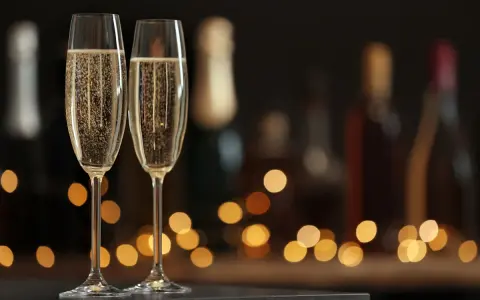 Zwei Sektgläser mit sprudelndem Sekt, im Hintergrund unscharfe Flaschen und Lichter. Ein krug 169 für besondere Anlässe.