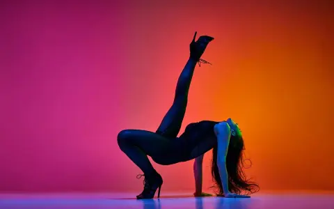 Tancerka w czarnym body i szpilkach wykonuje akrobatyczną figurę na tle gradientu różu i pomarańczy. High heels co to? To buty, które dodają pewności siebie.