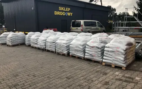 Palety z workami materiałów budowlanych przed sklepem drogowym.