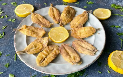 Deliciosos boquerones al limón, crujientes y dorados, servidos en un plato con rodajas de limón y perejil fresco.